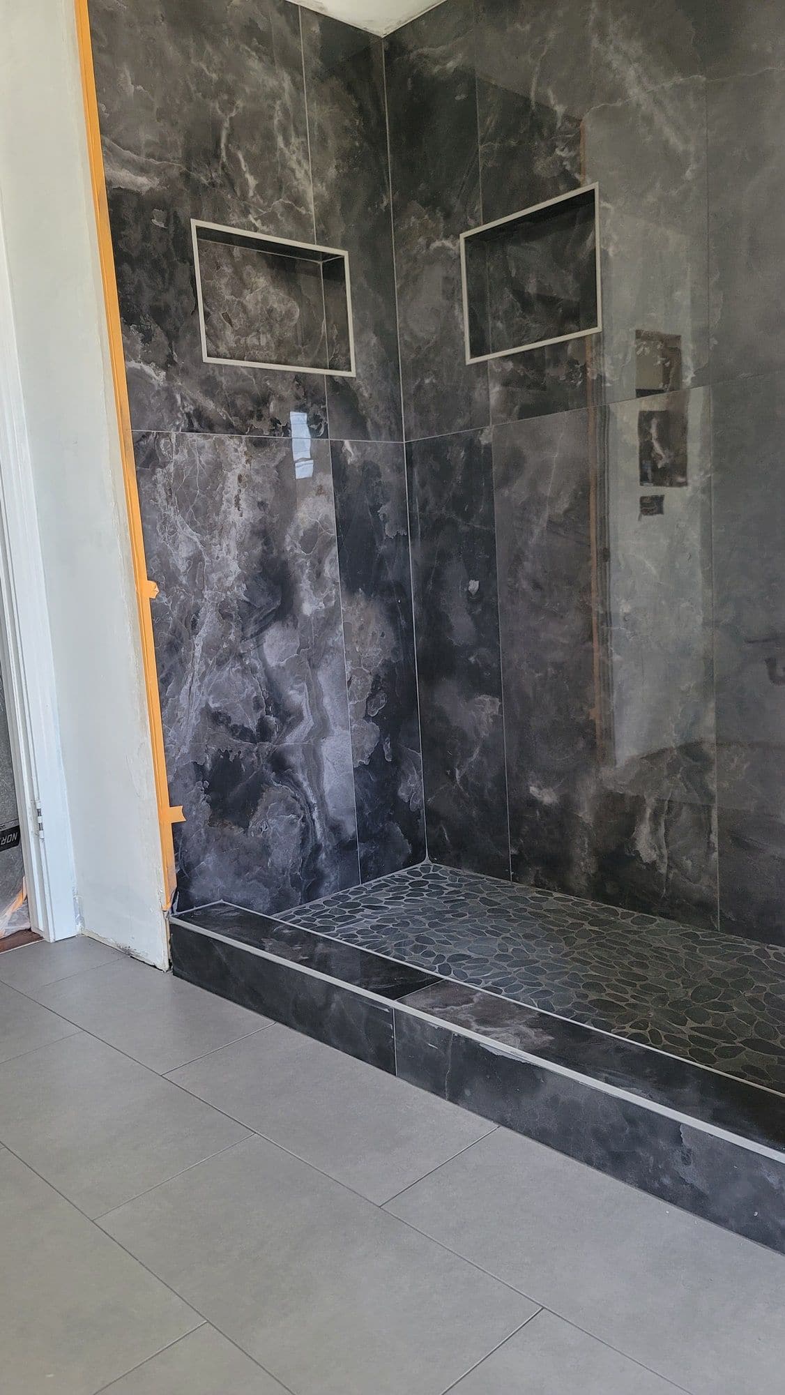 Dark marble tile shower surround with a tiled step, mid-installation